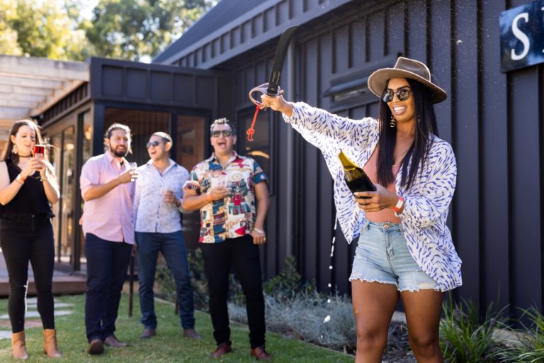 A woman removes the top of a sparkling wine bottle with a sabre.