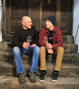 Father and son Dettweiler sit together infront of a door and taste wine