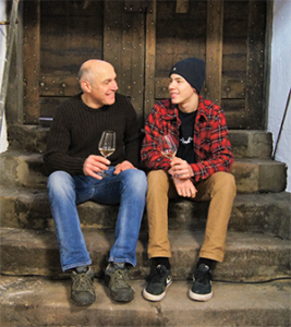 Two generations of winegrowers Father and son Dettweiler sit together infront of a door and taste wine